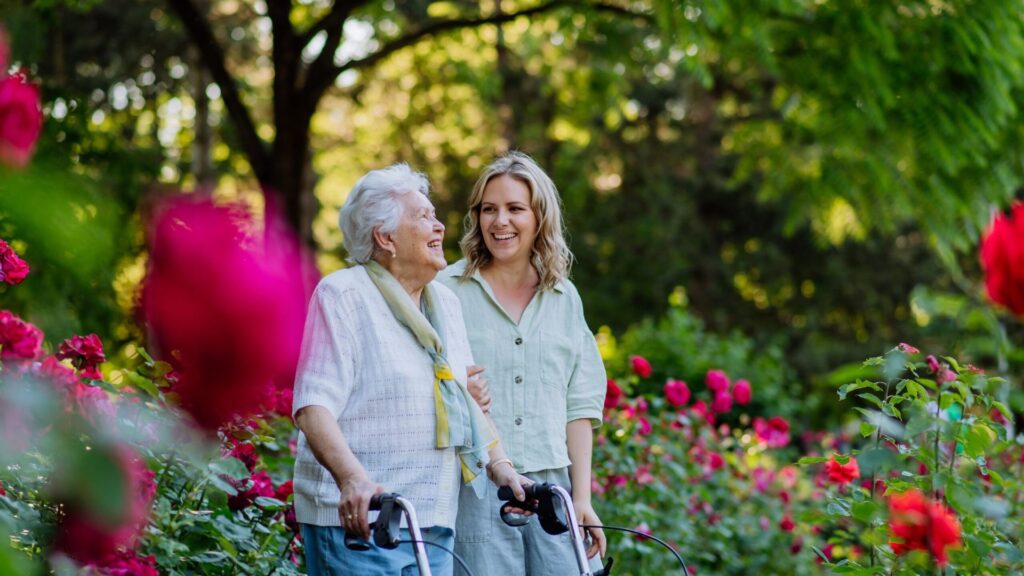 Home care companion assisting a woman walk through a park