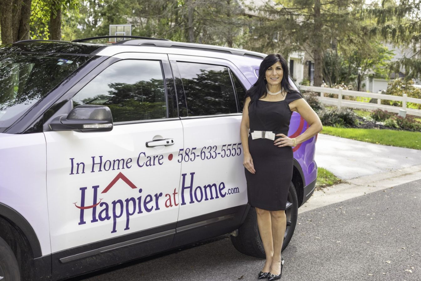 Debbie Marcello founder of home care franchisor Happier At Home standing next to a car wrapped with Happier At Home branding